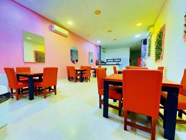 A dining area with multiple tables and orange chairs, a kitchen in the background, and a ceiling with recessed lighting. - Hotel Playa Norte (Cartagena)