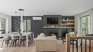 A modern living room with a fireplace, dining area, and a large window. - Le Panaché - Cottage to rent in Stoneham (CITQ: 298070) (Stoneham-et-Tewkesbury)