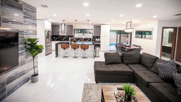 A modern kitchen with a central island, bar stools, and a dining area with a view of the outdoors.