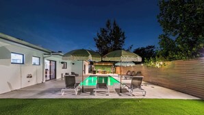 A backyard with a swimming pool, outdoor seating, and a covered area with umbrellas.