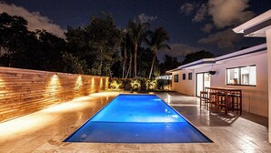 A swimming pool with a wooden deck and a white building with large windows.
