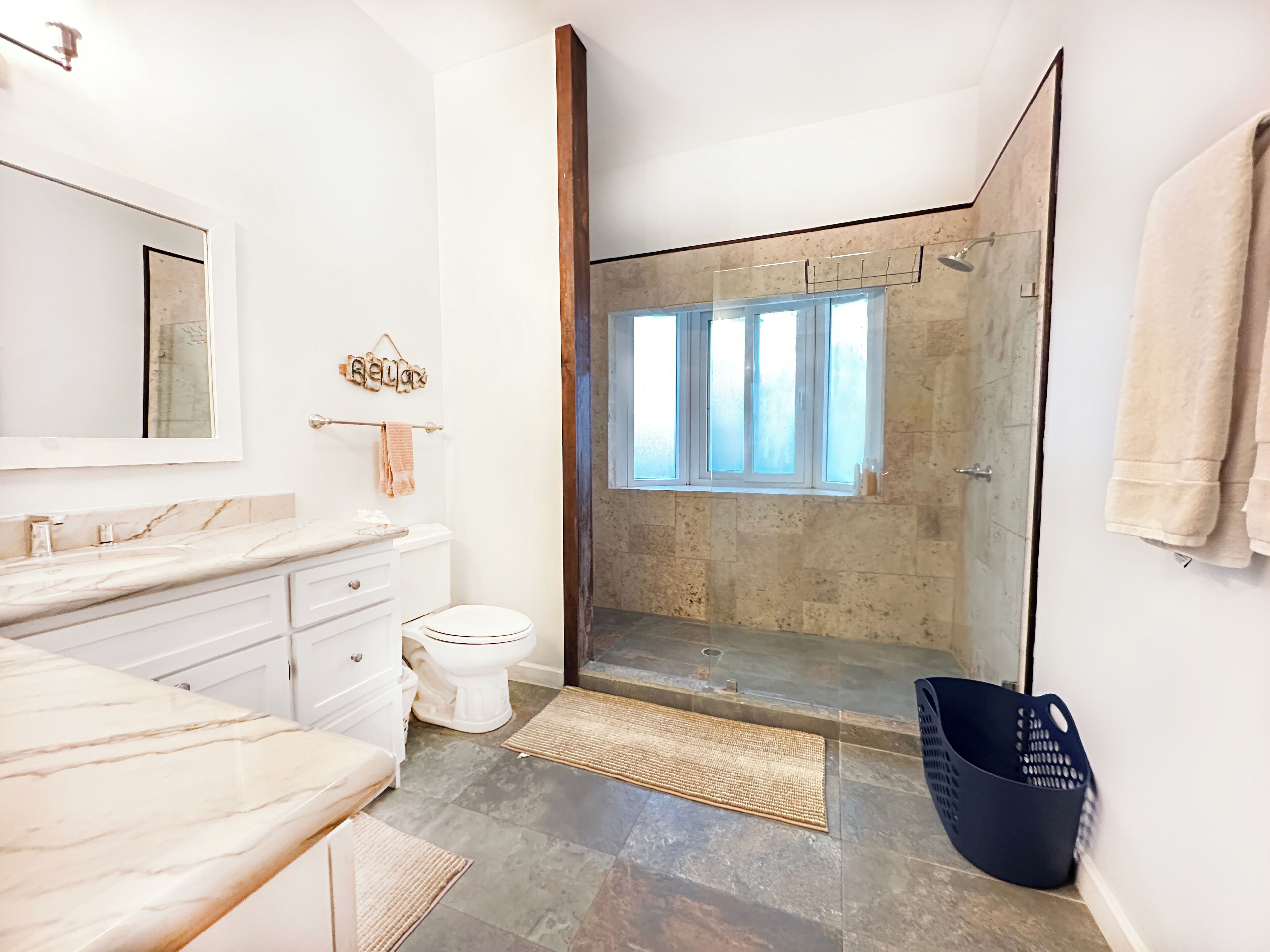 A modern bathroom with a marble vanity, a toilet, a glass-enclosed shower, and a large mirror.