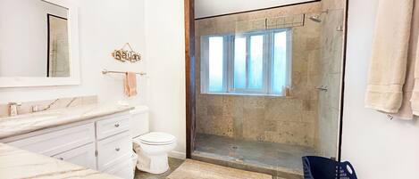 A modern bathroom with a marble vanity, a toilet, a glass-enclosed shower, and a large mirror.