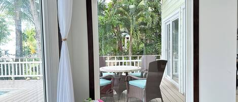 A room with a view of a wooden deck, a wicker chair with a cushion, and a white laundry basket.