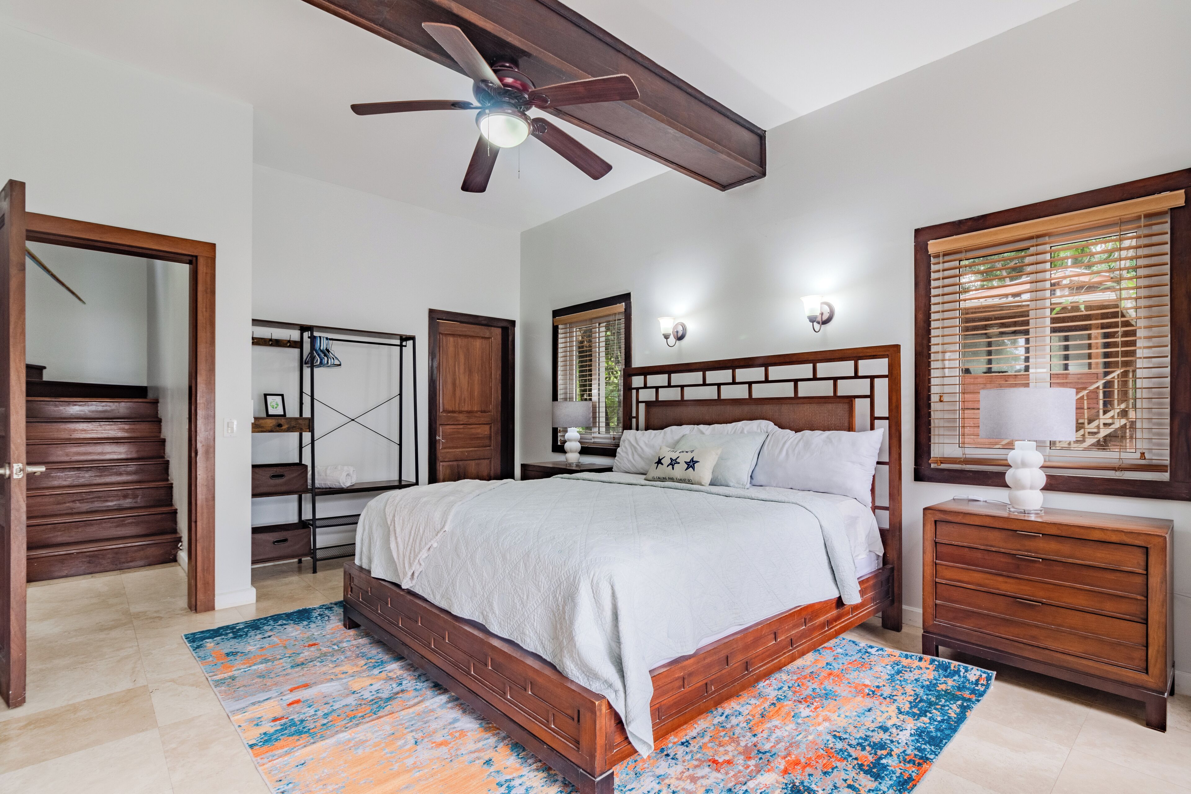 A bedroom with a wooden bed, a ceiling fan, a nightstand, and a window with blinds.