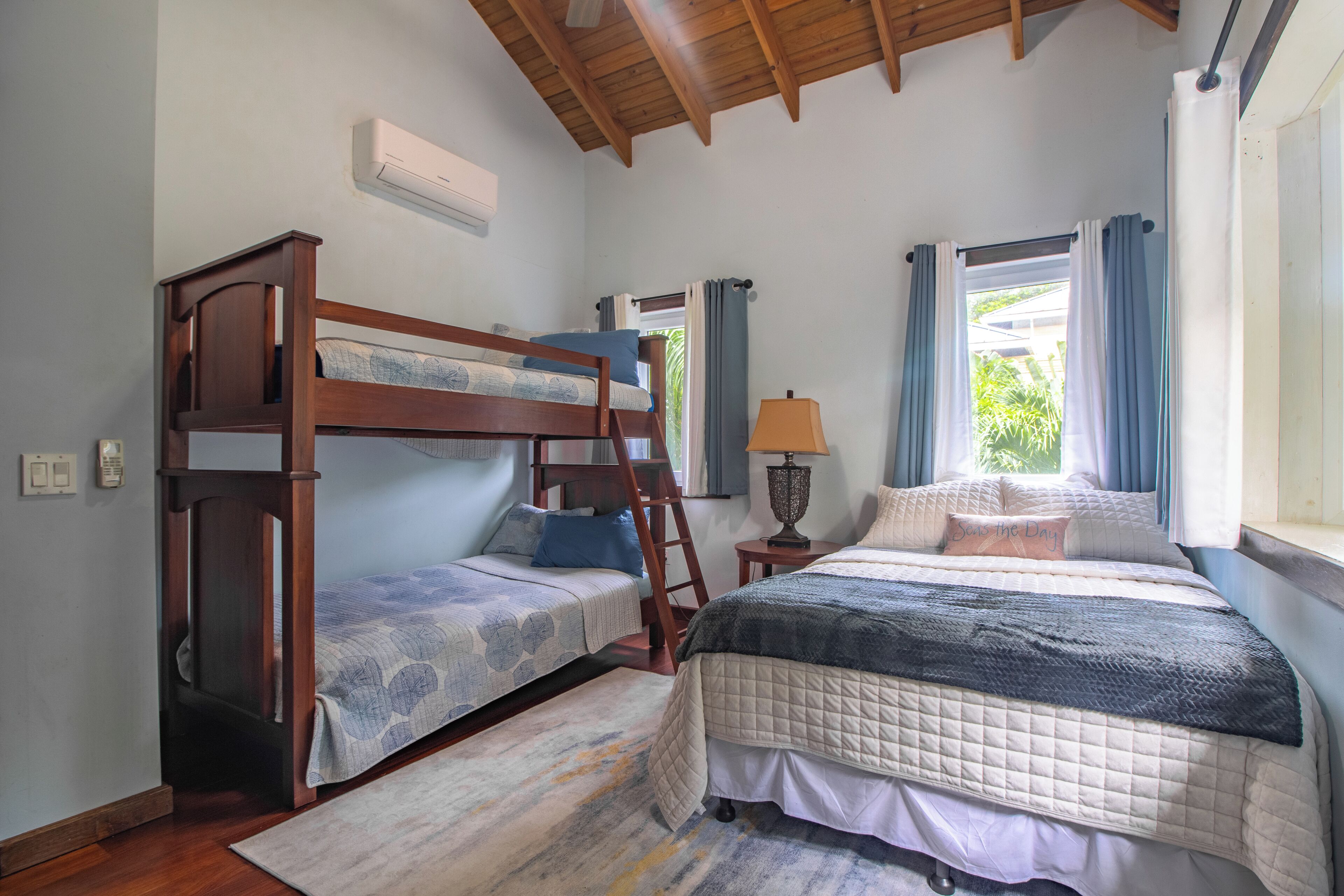 Ein Schlafzimmer mit Etagenbett, einem Einzelbett, einer Leiter, einer Lampe und einem Fenster mit Vorhängen.