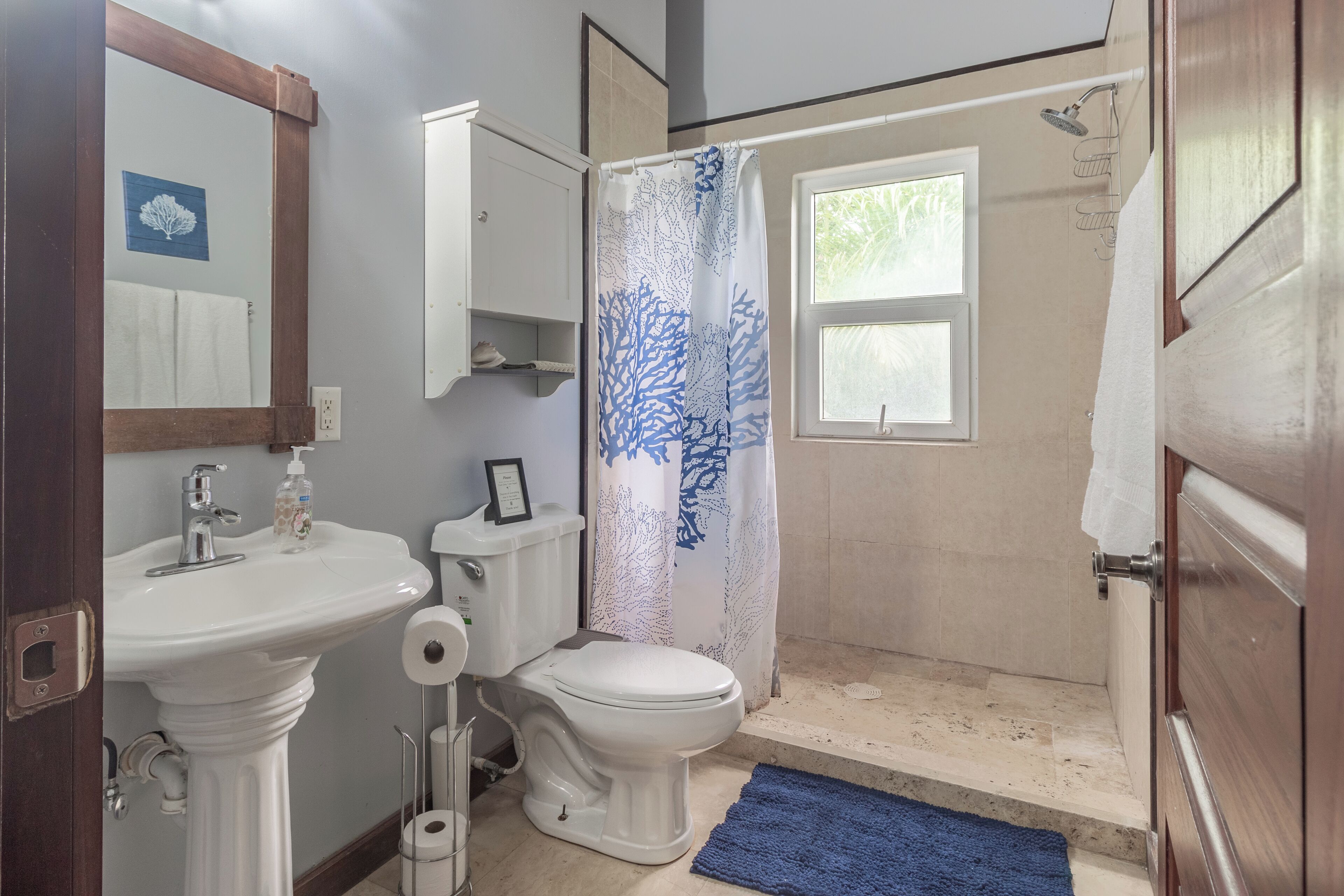A bathroom with a pedestal sink, toilet, and shower area.