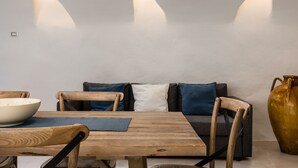 Un comedor con mesa de madera, sillas, un cuenco, un jarrón y un sofá con cojines.