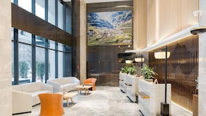 A spacious lobby with a modern design, featuring a large window, a reception desk, and seating areas.