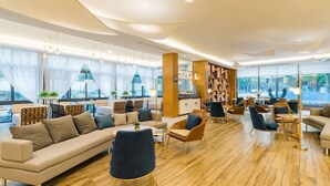 A modern hotel lobby with a large seating area, a reception desk, and a view of the outdoors.