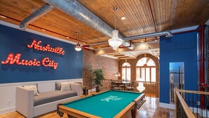 A pool table in a room with a neon sign reading "Nashville Music City," a sofa, and a staircase.