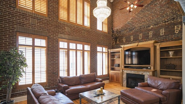 A spacious living room with leather sofas, a fireplace, and a large window with blinds.