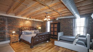 A bedroom with a wooden ceiling, brick walls, a bed, a sofa, and a wardrobe.