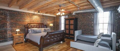 A bedroom with a wooden ceiling, brick walls, a bed, a sofa, and a wardrobe.