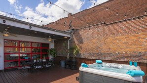 An outdoor patio with a hot tub, wooden deck, and brick wall.