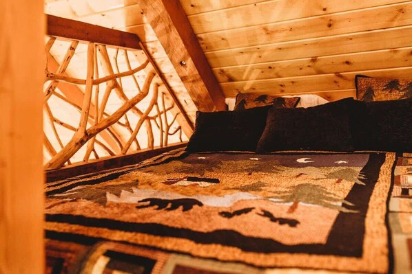 Un plafond en bois orné d’un motif en croisillons, un lit recouvert d’une couvre-lit à motifs et un oreiller de couleur sombre.