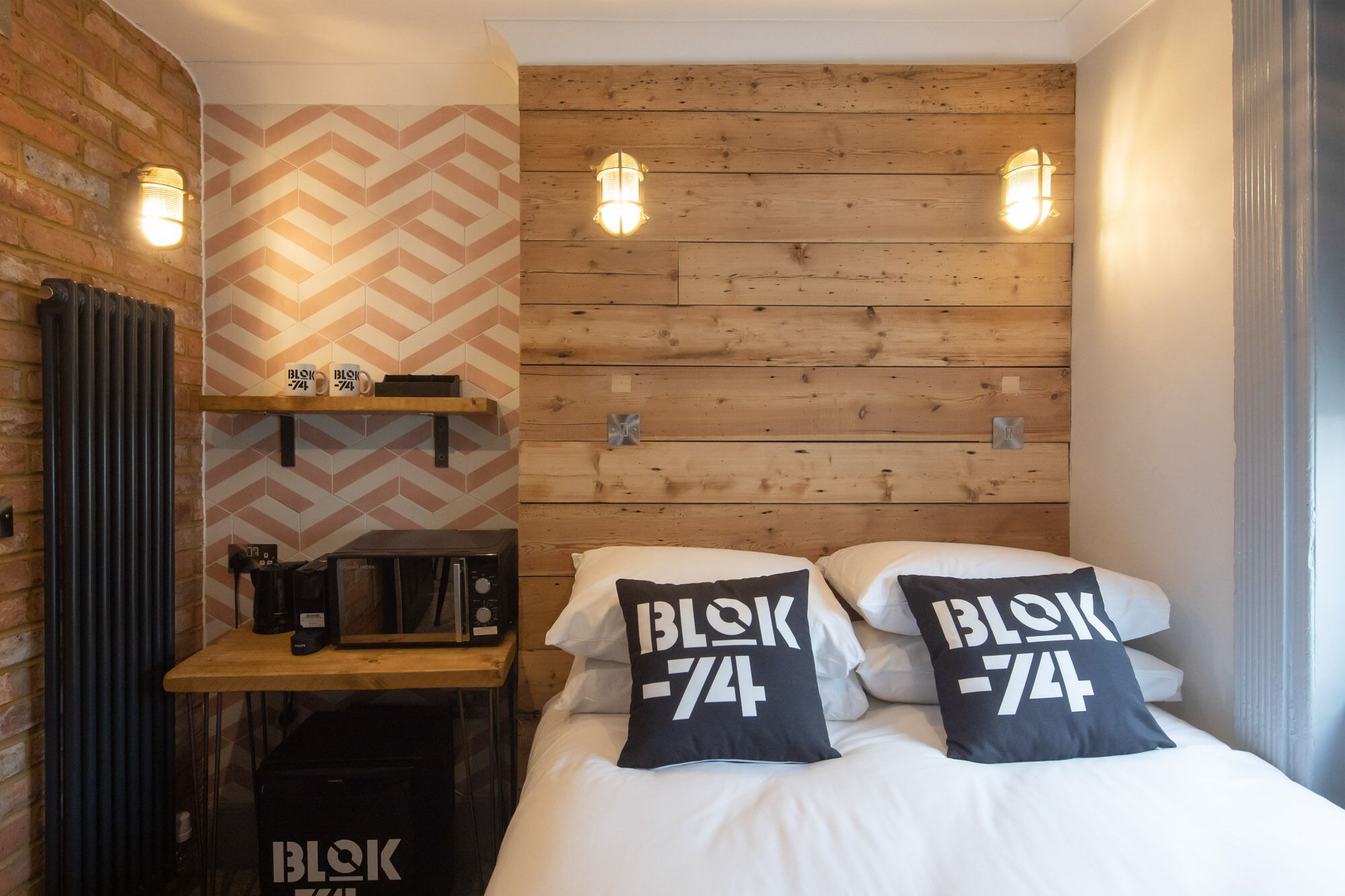 A cozy room with a wooden wall, a microwave on a shelf, and two pillows with 'BLOK-74' text.