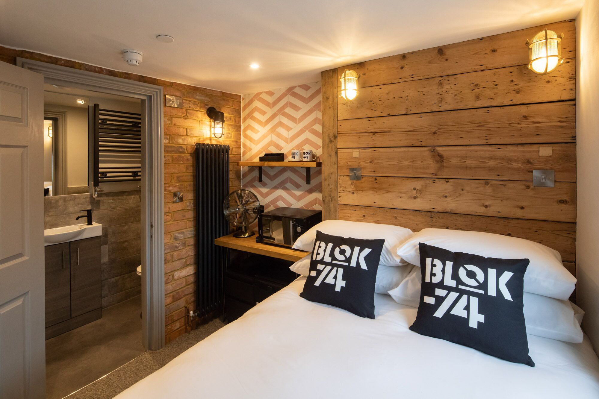 A bedroom with a wooden headboard, two pillows with 'blok 74' text, a bedside table, a radiator, and a mirror.