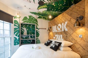 Un dormitorio moderno con cabecera de madera, un ventanal grande y un mural de hojas verdes.