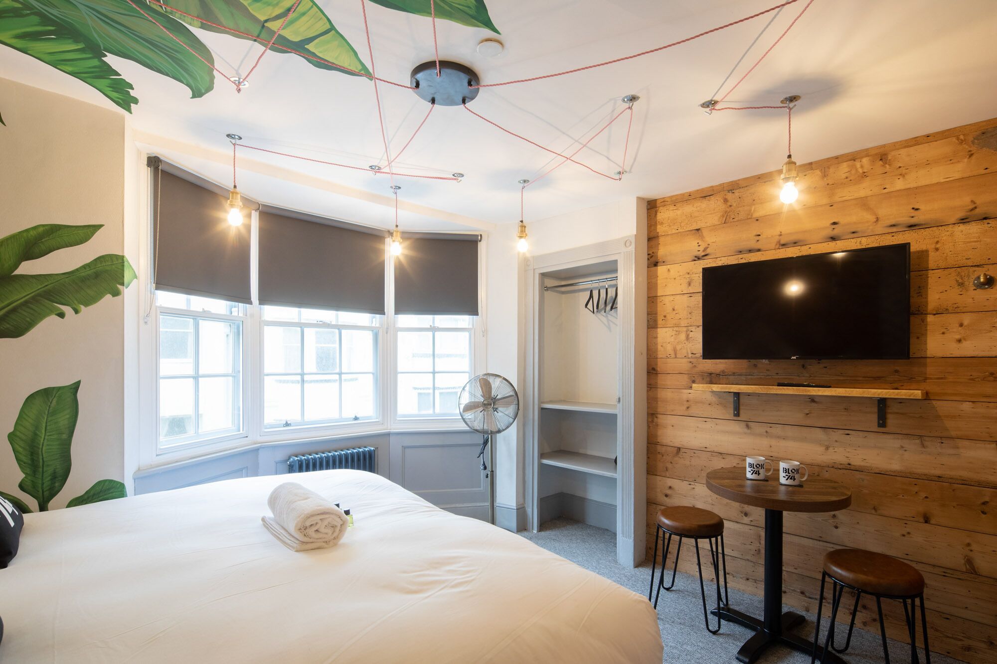 Une chambre d’hôtel avec un grand lit, un téléviseur fixé à un mur en bois, une petite table ronde avec des tabourets et une fenêtre donnant sur l’extérieur.