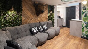 Un salón moderno con pared de madera, una cabeza de toro montada y un sofá con cojines estampados.