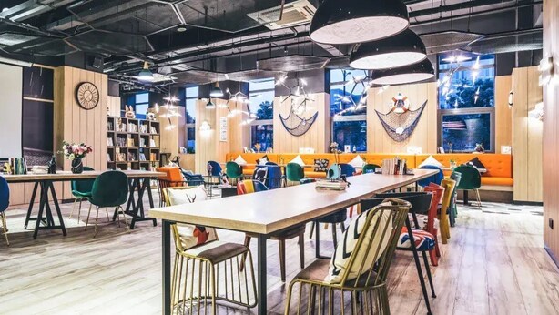 A modern co-working space with a long communal table, colorful chairs, and a variety of seating options. - Atour Light (Hangzhou)