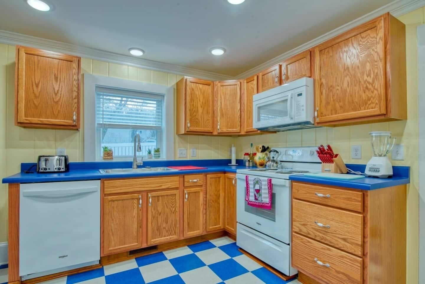A kitchen with wooden cabinets, a white stove, a microwave, a toaster, and a blue countertop.