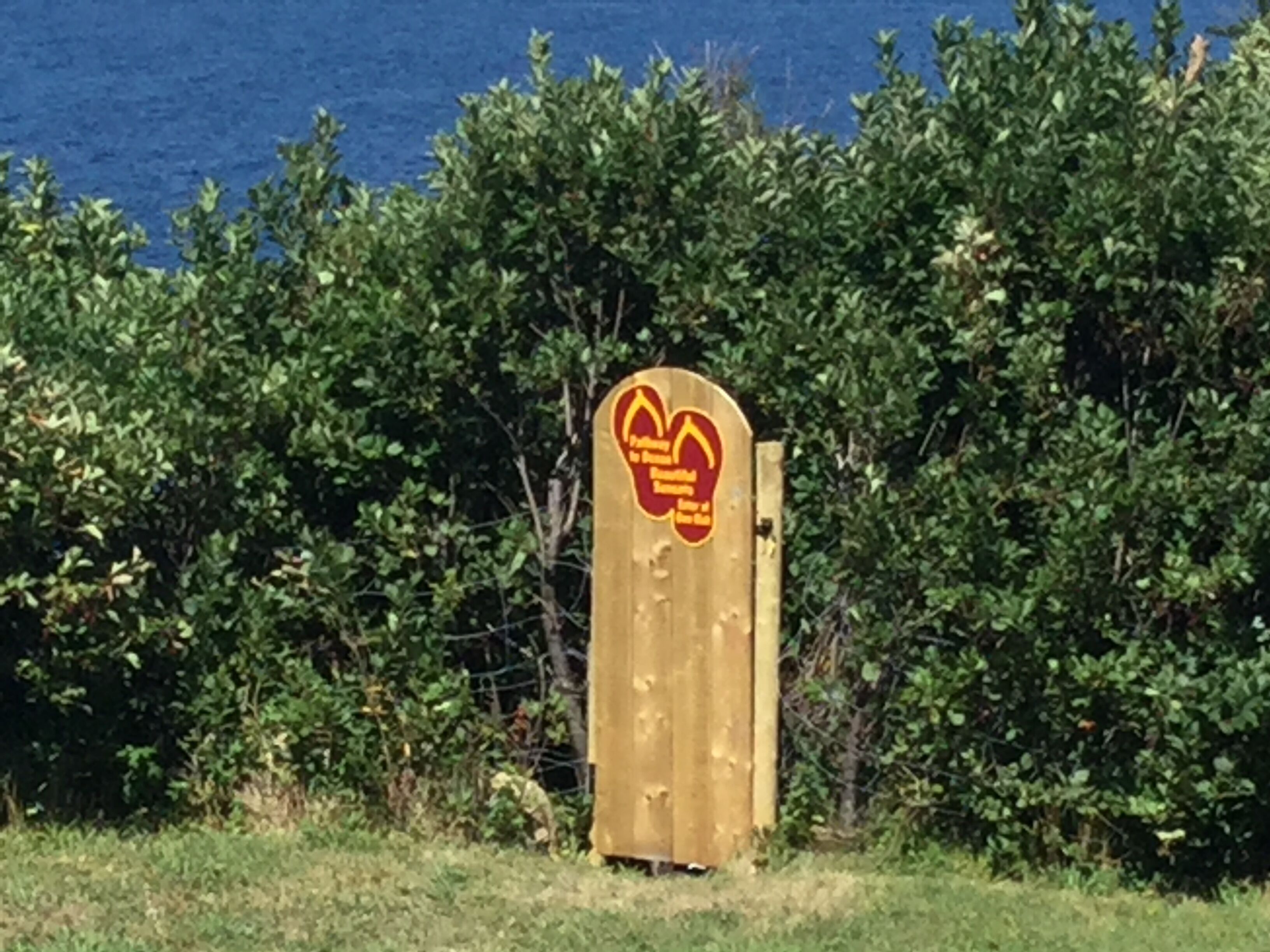A wooden gate with a circular sign featuring a logo and text, surrounded by dense green foliage.