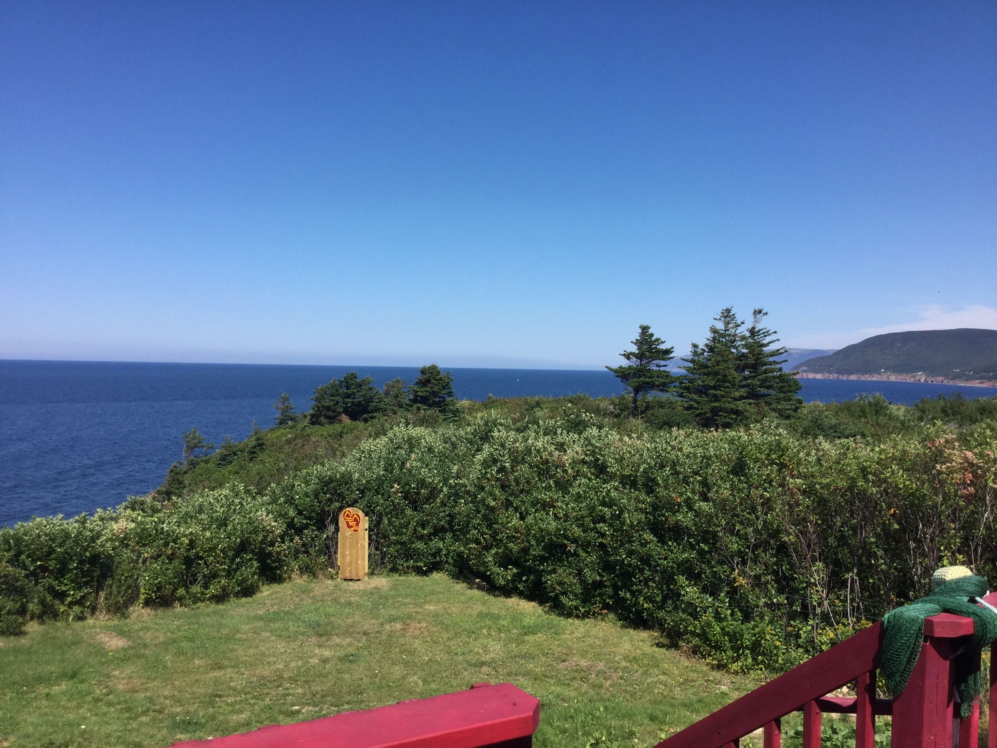 A coastal view with a grassy area, a wooden sign, and a red bench.