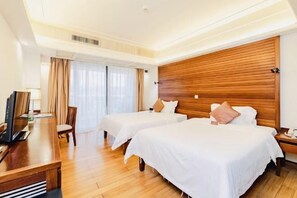 Une chambre d’hôtel avec deux lits, une tête de lit en bois, un bureau avec un ordinateur et une grande fenêtre avec des rideaux.