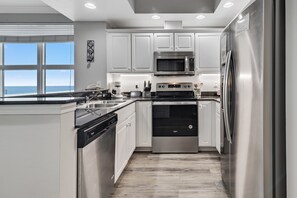 A modern kitchen with white cabinetry, stainless steel appliances, and a view to the ocean.