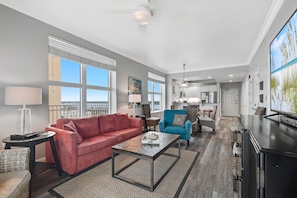 A spacious living room with a red sofa, a blue armchair, and a coffee table. There is a kitchen in the background with modern appliances.