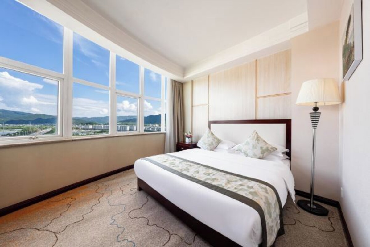 A hotel room with a large window offering a view of a cityscape and mountains.