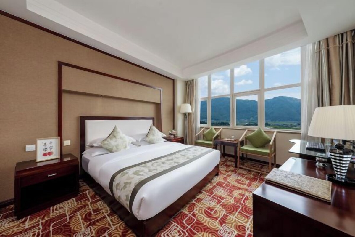Een hotelkamer met een groot bed, een bureau, een stoel en uitzicht op bergen door het raam.