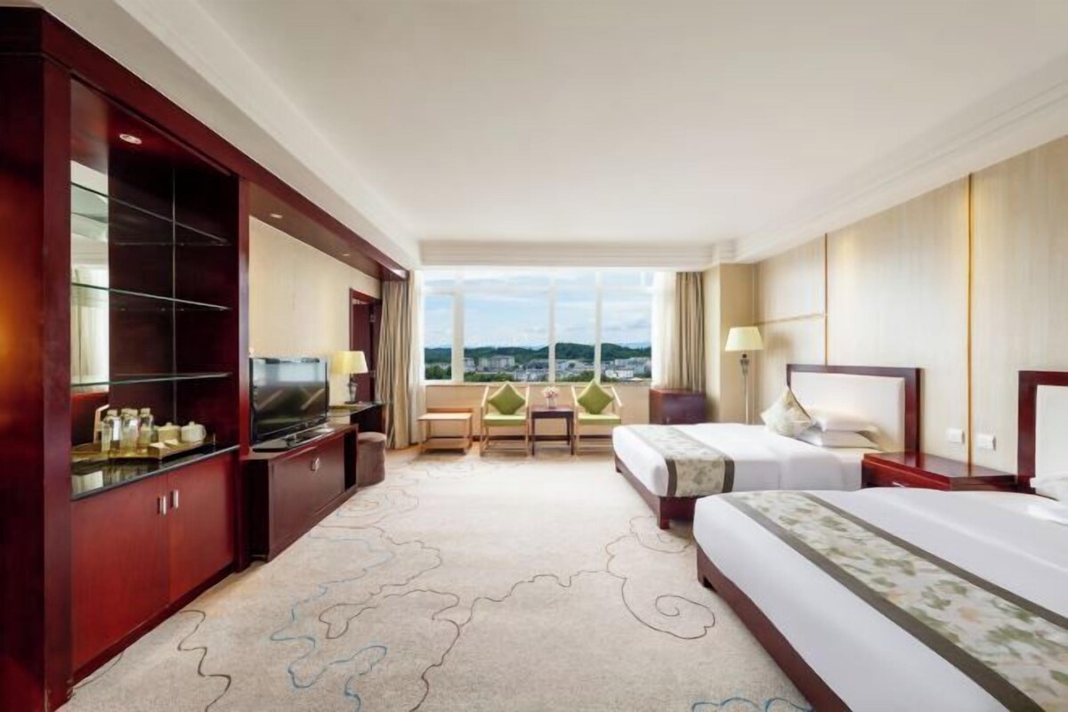 A hotel room with a large bed, a TV, a seating area with a view, and a large window.