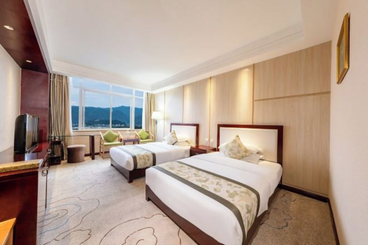 A hotel room with two beds, a desk, a TV, and a view of the mountains.