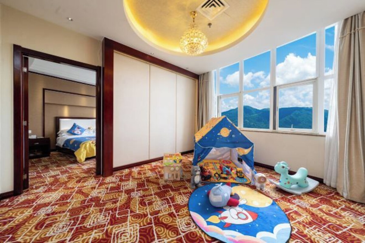 Una camera d'albergo con tappeto a motivi, un letto con copriletto blu e giallo, una piccola tenda da gioco e vista sulle montagne attraverso ampie finestre.