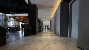 Moderni hotellikäytävä, jossa on marmorilattia, puuelementtejä ja sisätiloissa olevia kasveja.