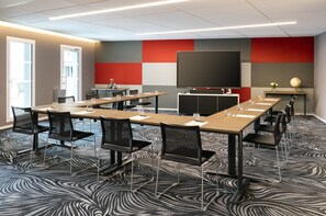 Una sala conferenze con una grande televisione a schermo piatto, diversi tavoli con sedie e una moquette decorata.