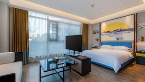 A modern hotel room with a large bed, a flat-screen TV, a glass coffee table, and a painting of a mountain landscape. - Bailing Hot Spring Hotel (Anshun)