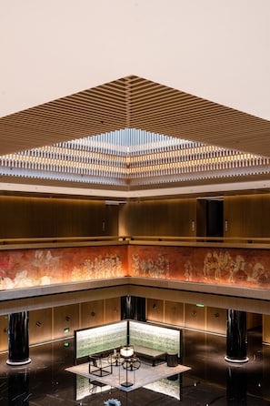 A spacious lobby with a high ceiling, a central seating area, and a large digital display.