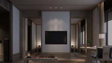 A modern hotel lobby with a large flat-screen TV mounted on a wall, a seating area with a round table and chairs, and a small side table with a lamp.