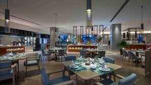 A modern dining area with multiple tables and chairs, a central bar, and a view of the cityscape. - Hongtang Bay Jianguo Resort Sanya (Sanya)