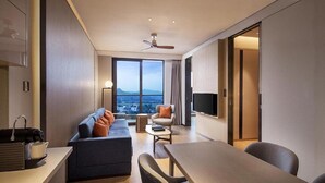A modern hotel room with a sofa, a dining table, a TV, and a large window offering a city view. - Hongtang Bay Jianguo Resort Sanya (Sanya)