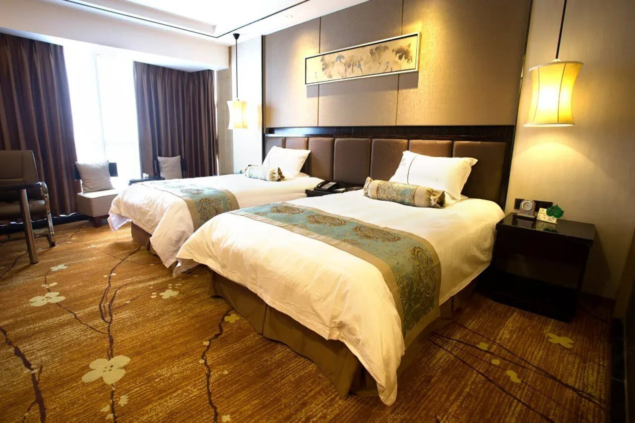 Ein Hotelzimmer mit zwei Betten, einem Schreibtisch, einem Stuhl, einem Nachttisch und einem großen Fenster mit Vorhängen.