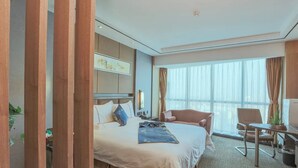 Una habitación de hotel con una cama grande, un escritorio, una silla y una ventana con cortinas.