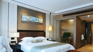 Una habitación de hotel con una cama grande, una mesita de noche con lámpara, una obra de arte en la pared y una planta en maceta.