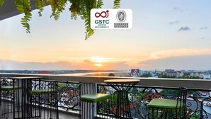 A balcony with a view of a sunset over a cityscape, a table, and two chairs. - Surestay Hotel by Best Western Vientiane (Vientiane)