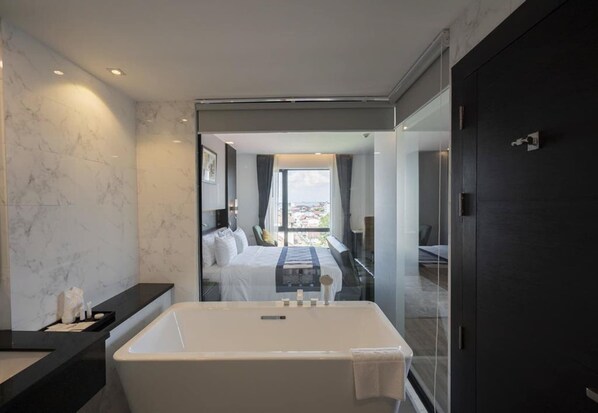 A modern bathroom with a large bathtub, a glass shower enclosure, and a view of the city through the window.