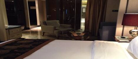 A hotel room with a large bed, a desk, a chair, and a mirror.